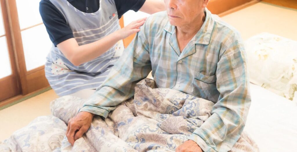寝たきり老人の背中をさする女性ヘルパーの無料の写真素材
