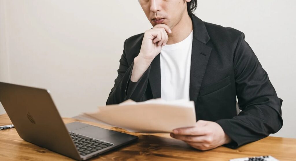 「ほうほう」顎に手を添えて資料を見る男性の無料の写真素材